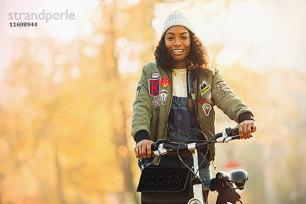 Portrait lächelnde junge Frau mit Fahrrad vor Herbstbäumen