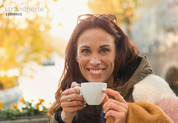 Portrait lächelnde Frau beim Kaffeetrinken im herbstlichen Straßencafé