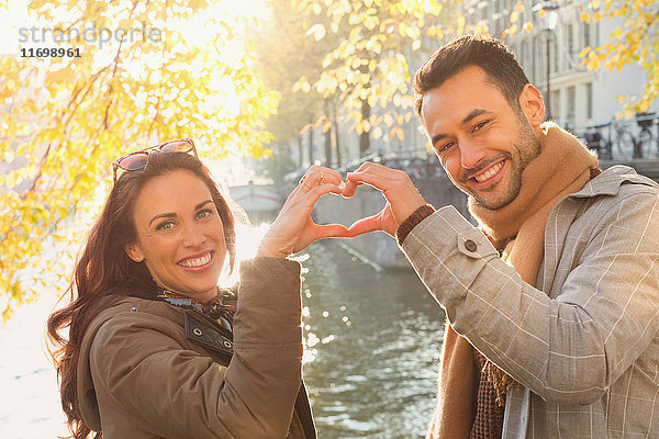 Portrait lächelndes junges Paar in Herzform mit Händen am sonnigen Herbstkanal