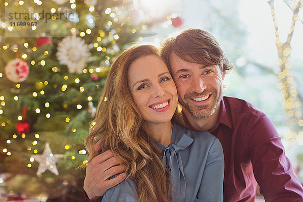 Porträt lächelndes Paar  das sich vor einem Weihnachtsbaum umarmt