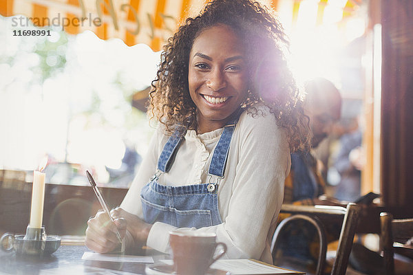 Portrait lächelnde junge Frau beim Kaffeetrinken und Postkartenschreiben im Café