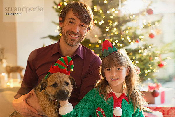 Portrait lächelnder Vater  Tochter und Hund vor dem Weihnachtsbaum