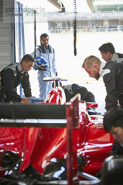 Formel-1-Fahrer beobachtet Boxencrew bei der Arbeit am Rennwagen in der Reparaturwerkstatt