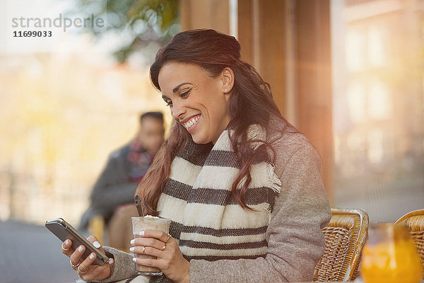 Lächelnde Frau beim SMSen mit Handy und Trinken von Milchshake im Straßencafé