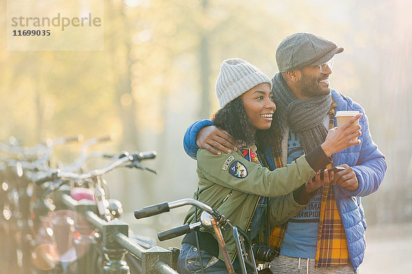 Junges Paar mit Fahrrad  das Kaffee trinkt und am Herbstgeländer entlang schaut  Amsterdam