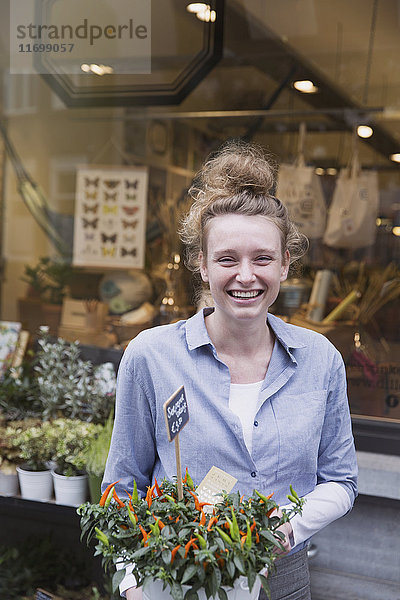 Porträt einer lächelnden Blumenhändlerin  die eine Topfpflanze im Schaufenster hält