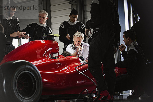 Manager und Boxencrew bei der Arbeit am Formel-1-Rennwagen in der dunklen Reparaturwerkstatt