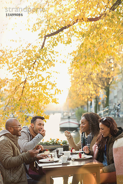 Freunde essen Dessert und trinken Kaffee im Herbst Bürgersteig Cafe entlang des Kanals