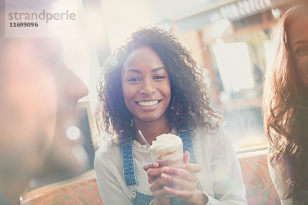 Portrait lächelnde junge Frau trinkt Milchshake mit Freunden im Cafe