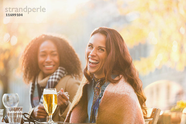 Portrait lachende junge Frauen Freunde beim Biertrinken im herbstlichen Straßencafé