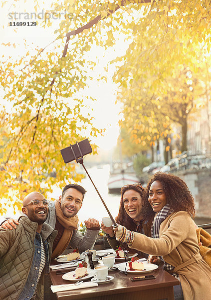 Lächelnde Freunde nehmen Selfie mit Selfie-Stick im herbstlichen Bürgersteig-Café