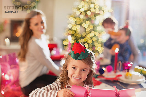 Porträt eines lächelnden Mädchens  das am Esstisch einen Weihnachtscracker hält