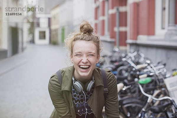 Porträt einer begeisterten  lachenden jungen Frau mit Kopfhörern auf einer Straße in der Stadt
