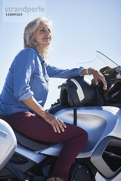 Lächelnde Seniorin auf dem Motorrad sitzend  wegschauend