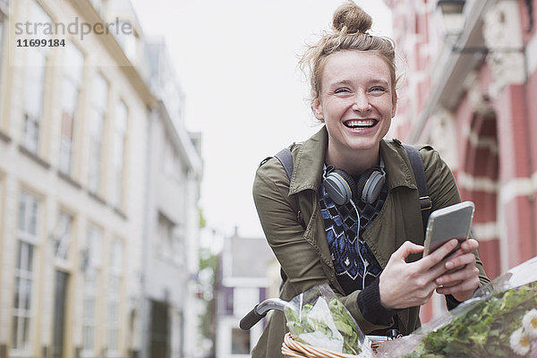 Porträt einer begeisterten jungen Frau auf dem Fahrrad  die auf einer Stadtstraße eine SMS schreibt