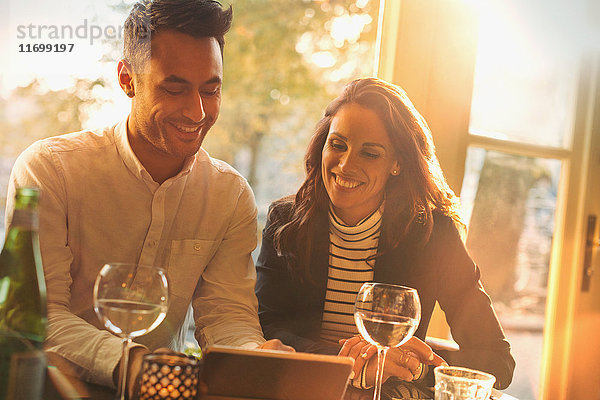 Junges Paar trinkt Wein und benutzt Tablet PC im sonnigen Restaurant