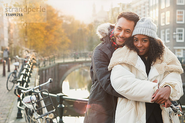 Portrait lächelndes junges Paar in warmer Kleidung am Kanal in Amsterdam
