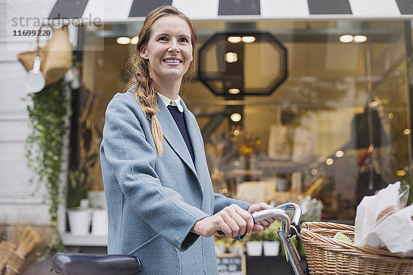 Portrait lächelnde Frau mit Fahrrad beim Schaufensterbummel