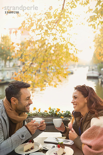 Junges Paar trinkt Kaffee und isst Käsekuchen-Dessert im herbstlichen Straßencafé entlang des Kanals.