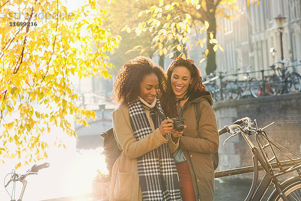 Lächelnde junge Frauen mit Digitalkamera am sonnigen städtischen Herbstkanal  Amsterdam
