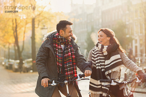 Lächelndes junges Paar in warmer Kleidung Fahrrad fahren auf urbaner Herbststraße