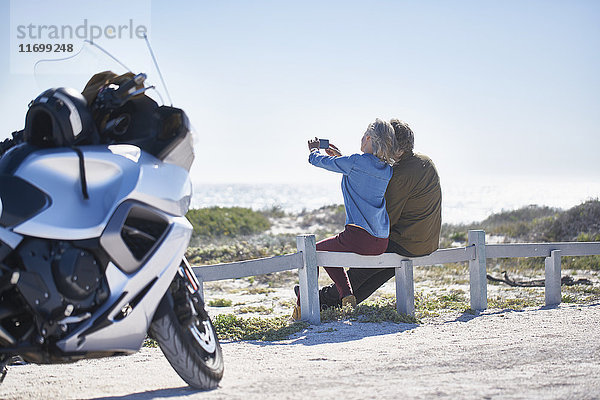 Seniorenpaar nimmt Selfie am sonnigen Straßenrand in der Nähe von Motorrad