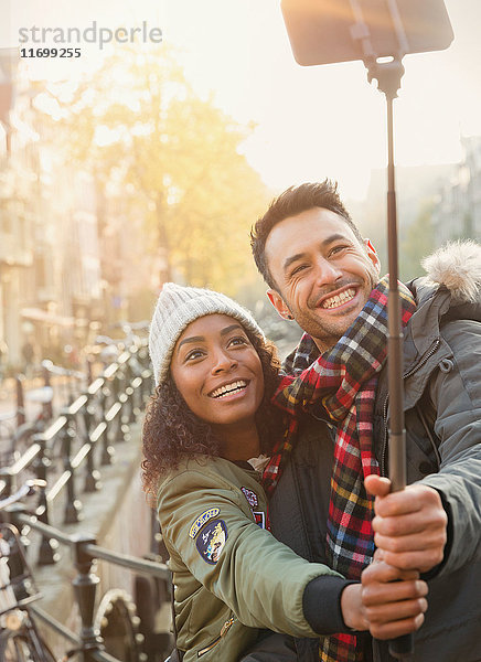 Lächelndes junges Paar  das Selfie mit Selfie-Stick auf der Straße nimmt.