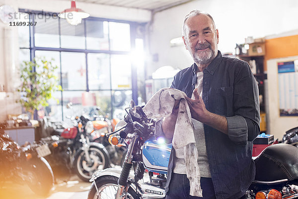 Portrait lächelnder Senior-Motorradmechaniker beim Händewischen in der Werkstatt