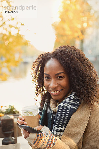 Portrait lächelnde junge Frau trinkt Kaffee und SMS mit Handy im städtischen Straßencafé