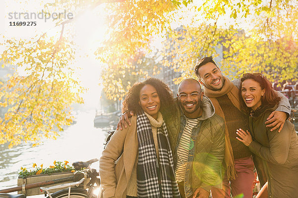 Portrait lächelnde Freunde beim Umarmen am sonnigen Herbstkanal