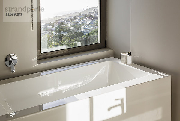 Sonnige Reflexion über moderner weißer Badewanne unter dem Fenster