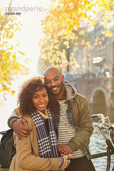 Porträt lächelndes  liebevolles Paar am sonnigen Herbstkanal umarmend