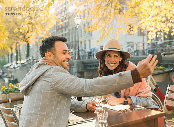 Junges Paar nimmt Selfie mit Fotohandy im herbstlichen Bürgersteig-Café