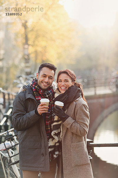 Portrait lächelndes junges Paar beim Kaffeetrinken am städtischen Herbstkanal