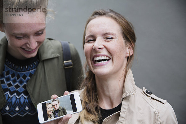 Lachende junge Frauen zeigen Selfie-Foto auf Smartphone