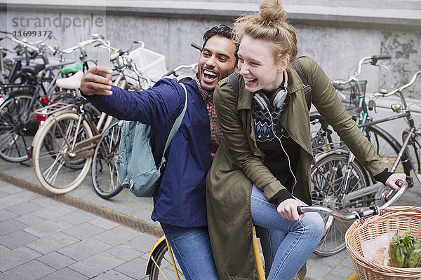 Verspieltes  lachendes junges Paar macht Selfie mit Fotohandy auf dem Fahrrad