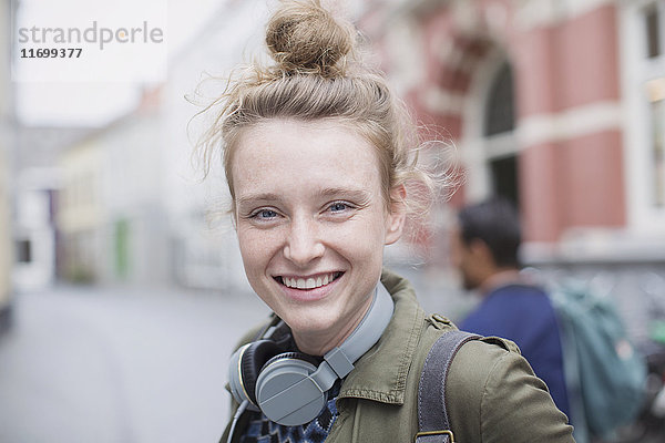 Porträt lächelnde junge Frau mit Kopfhörern auf der Straße in der Stadt