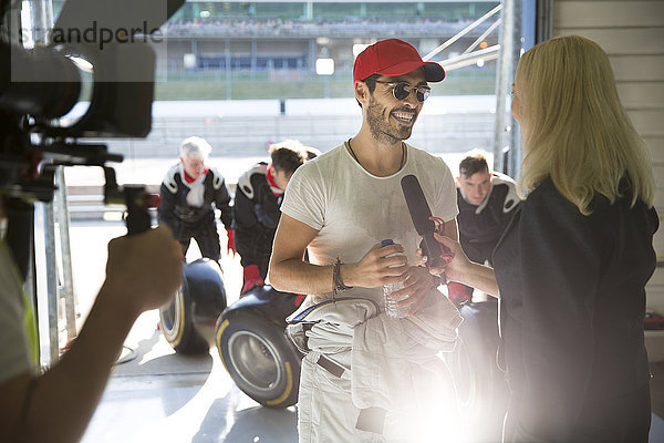 Weibliche Reporterin interviewt männliche Formel-1-Rennfahrer in der Reparaturwerkstatt