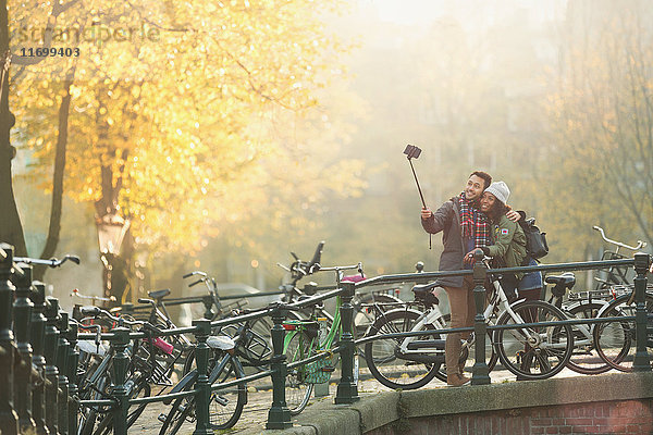 Junges Paar mit Fahrrädern nimmt Selfie mit Selfie-Stick auf der Herbstbrücke  Amsterdam