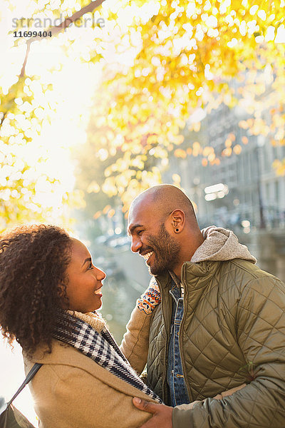 Lächelndes  anhängliches junges Paar  das sich unter einem sonnigen Herbstbaum umarmt