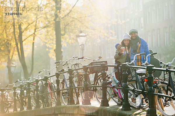 Portrait lächelndes junges Paar beim Kaffeetrinken entlang von Fahrrädern auf der sonnigen urbanen Herbstbrücke  Amsterdam