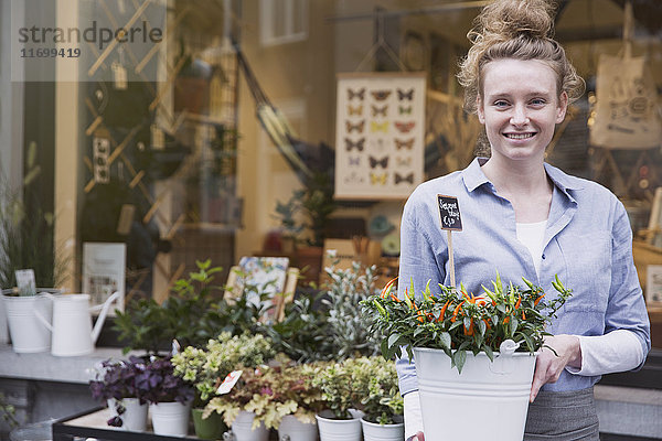 Porträt einer lächelnden Blumenhändlerin mit Topfpflanze im Schaufenster