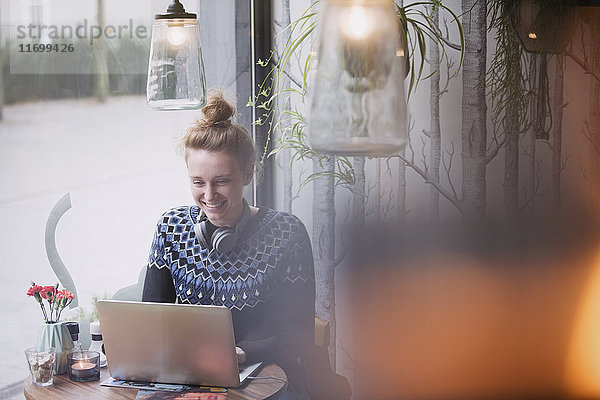 Lächelnde junge Frau mit Laptop in einem Caféfenster