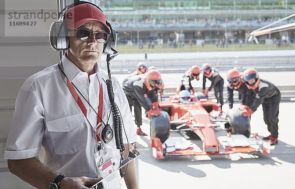 Portrait seriöser Manager mit Formel 1 Rennwagen und Boxencrew im Hintergrund