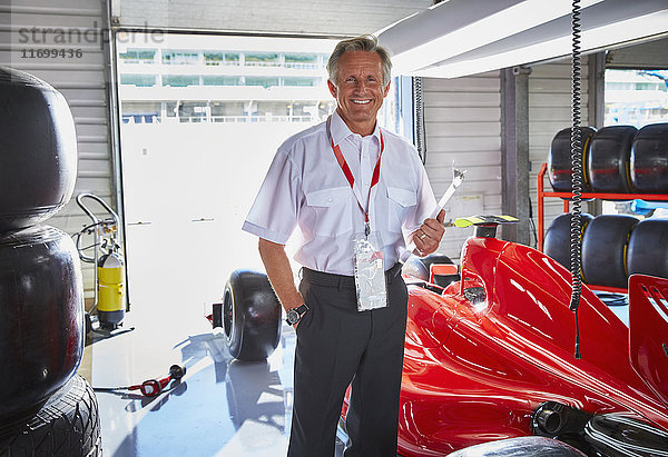 Porträt souveräner Formel-1-Manager neben dem Rennwagen in der Werkstatt
