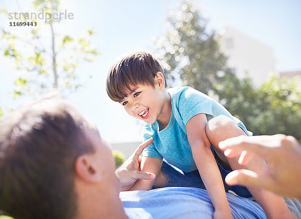 Lachender Sohn liegt auf dem Vater auf der sonnigen Terrasse.