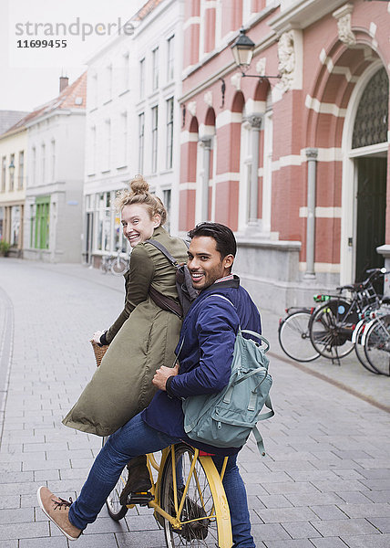 Porträt lächelnder junger Mann und Frau beim Fahrradfahren auf einer Stadtstraße