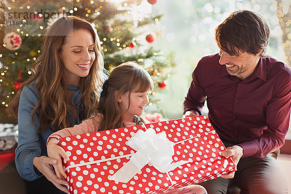 Eltern schenken ihrer Tochter ein großes Weihnachtsgeschenk vor dem Weihnachtsbaum