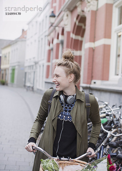 Lächelnde junge Frau mit Kopfhörern auf dem Fahrrad auf einer Straße in der Stadt
