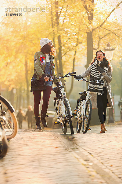 Junge Frauen  die mit dem Fahrrad durch die sonnige Herbststraße laufen.